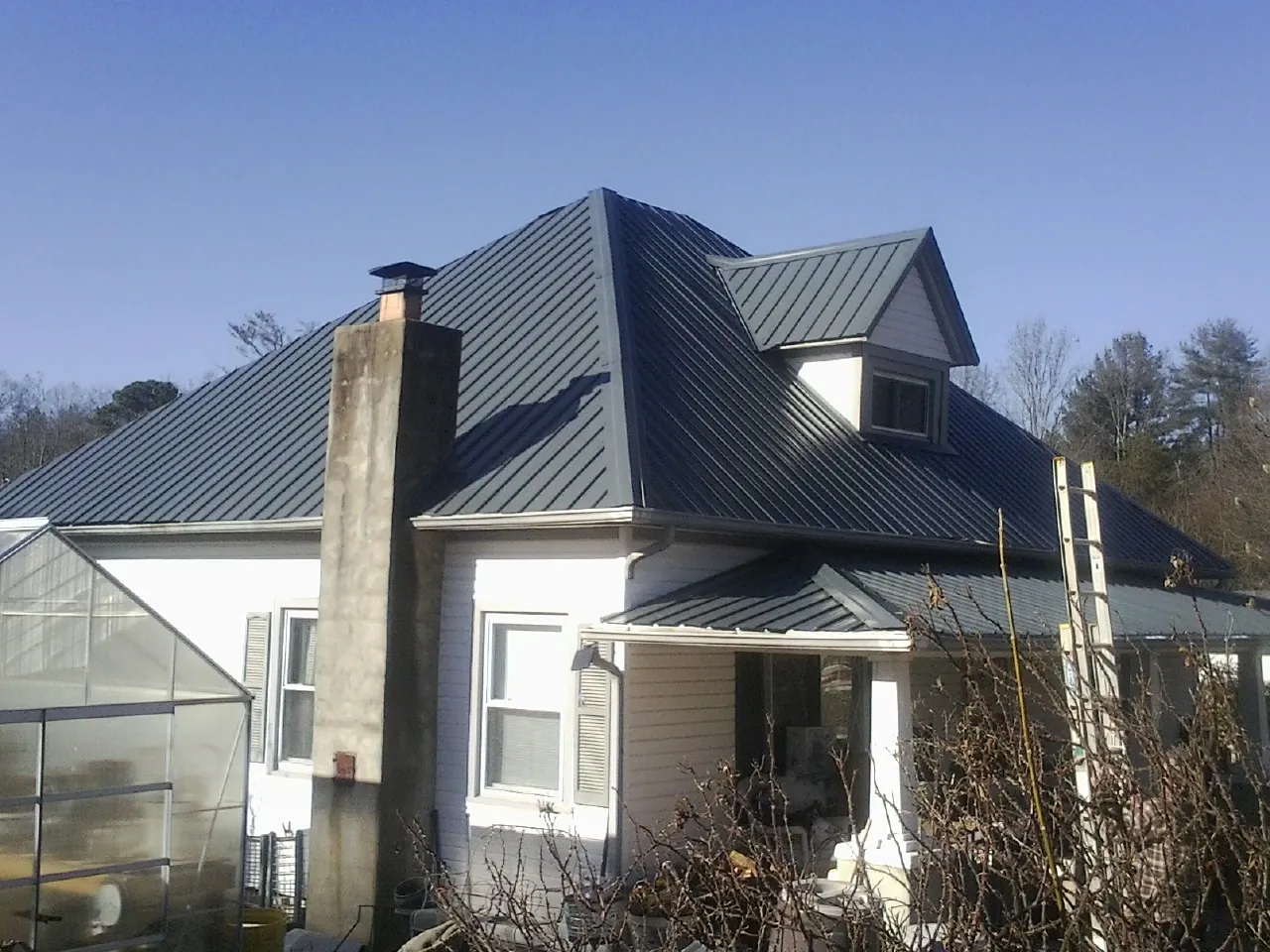 Dark blue standing seam metal roof on a white farmhouse with dormer — Slate & Tile Roof Repair by Roofing Brothers in Smithfield
