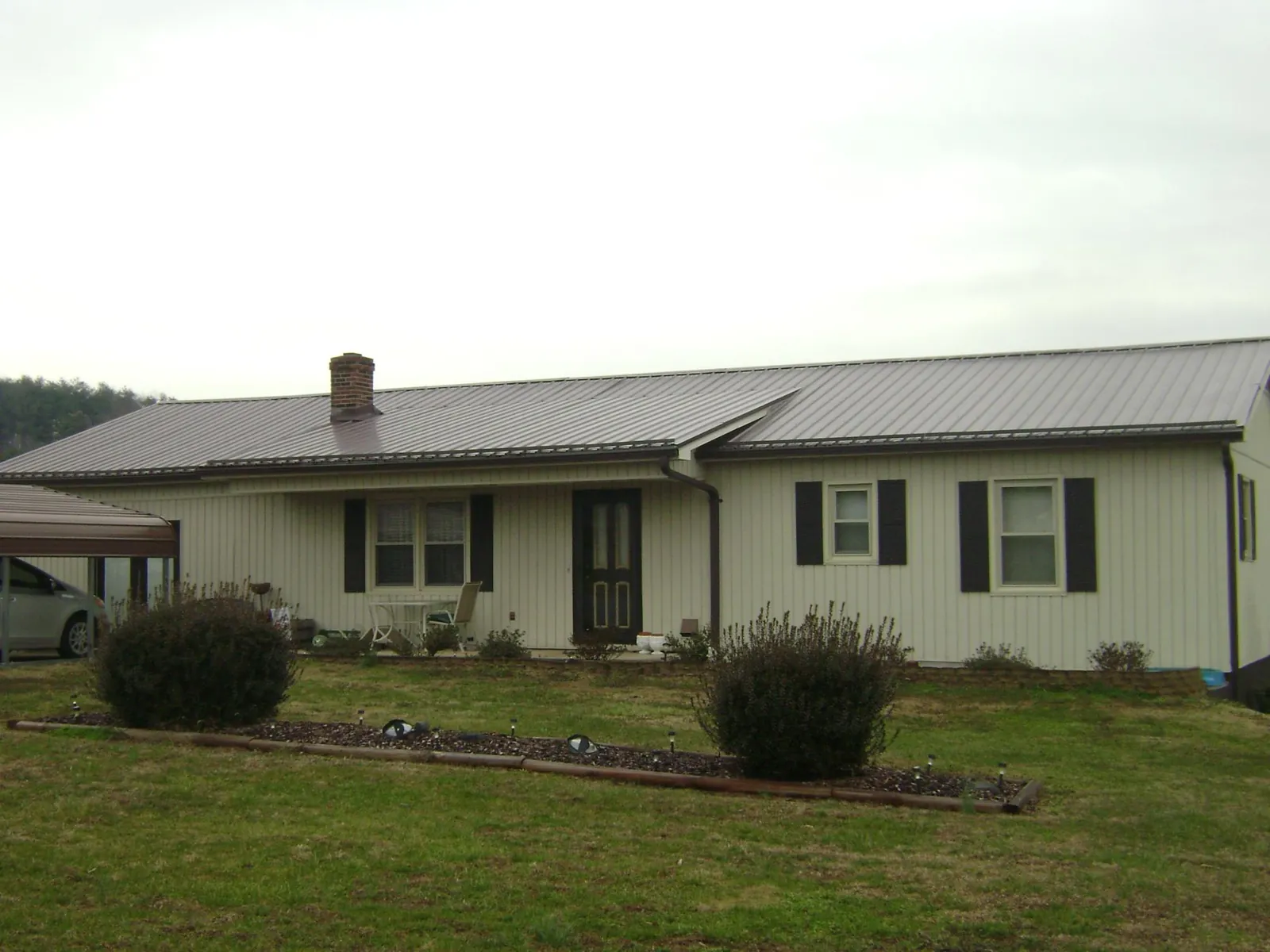 Brown metal roof on a cream sided ranch home with a brick chimney in Smithfield
